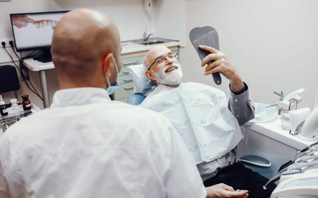 Paciente está recostado en la camilla, sonríe y mira sus dientes en el espejo, acudió a Maxorl para implantología avanzada en Málaga