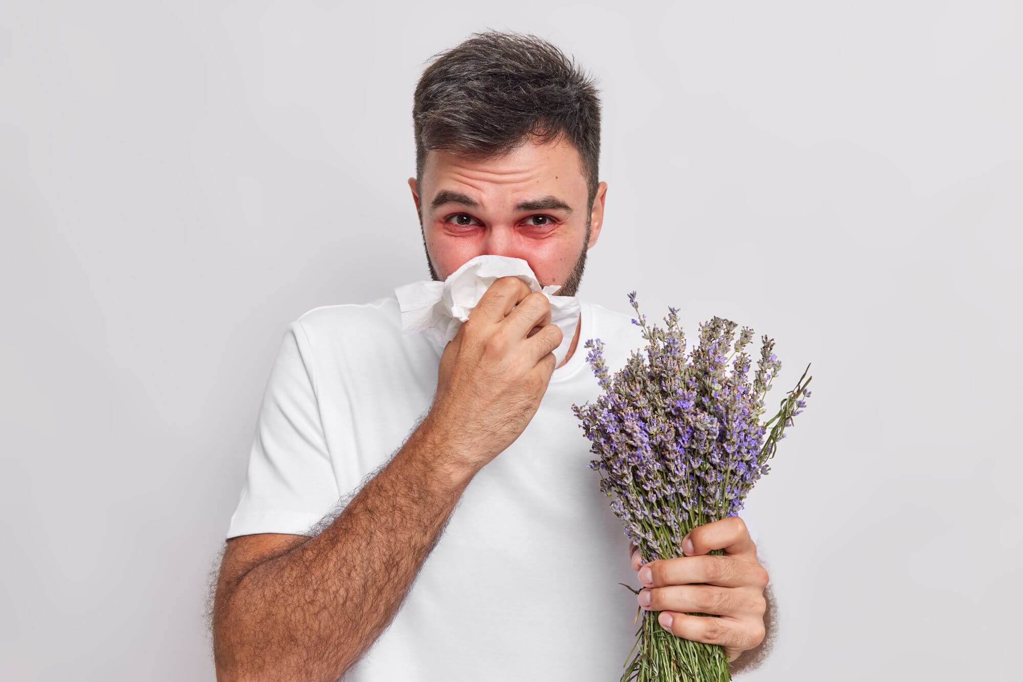 Joven sostiene ramo de lavanda mientras con el pañuelo se limpia la nariz porque tiene alergia